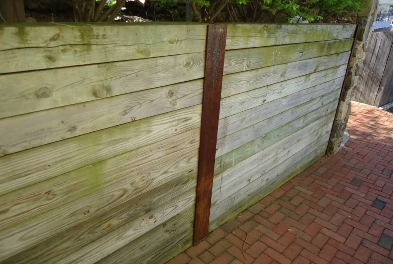 Timber retaining wall with steel posts beside a paved path